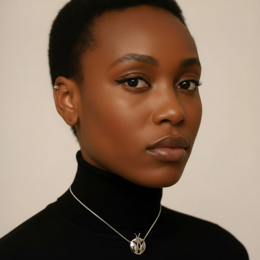 Woman wearing a black turtleneck and a necklace with a pendant against a neutral background